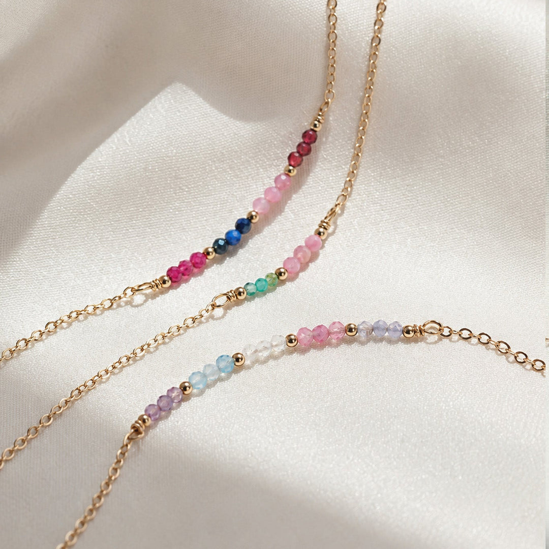Two beaded necklaces with gold chains on a light fabric background