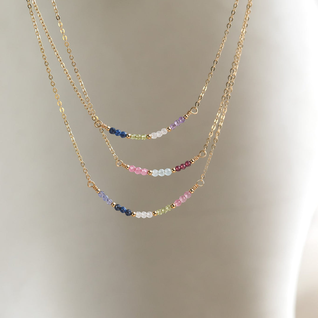 Gold chain necklace with colorful beads on a neutral background
