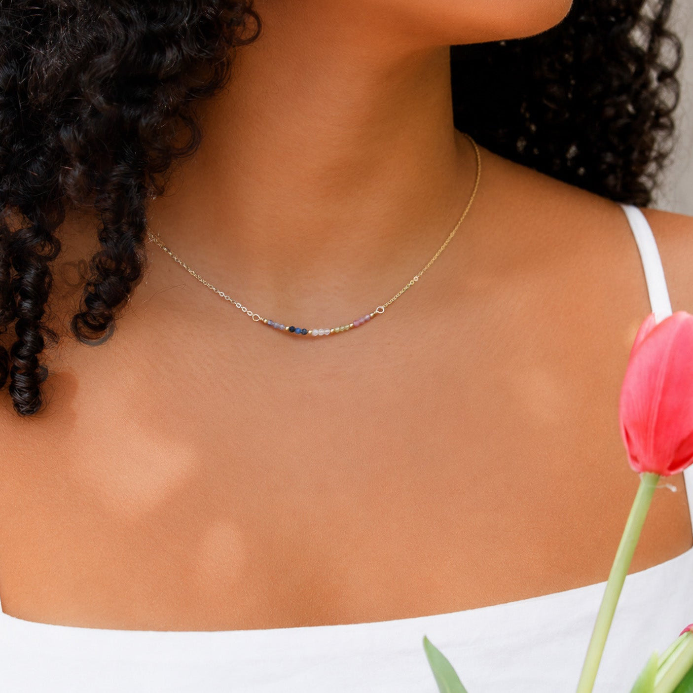 Woman wearing a gold necklace with a pink tulip in the foreground