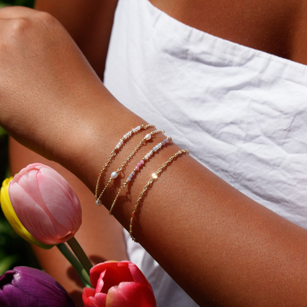 Close-up of a person's arm with gold bracelets holding tulips.