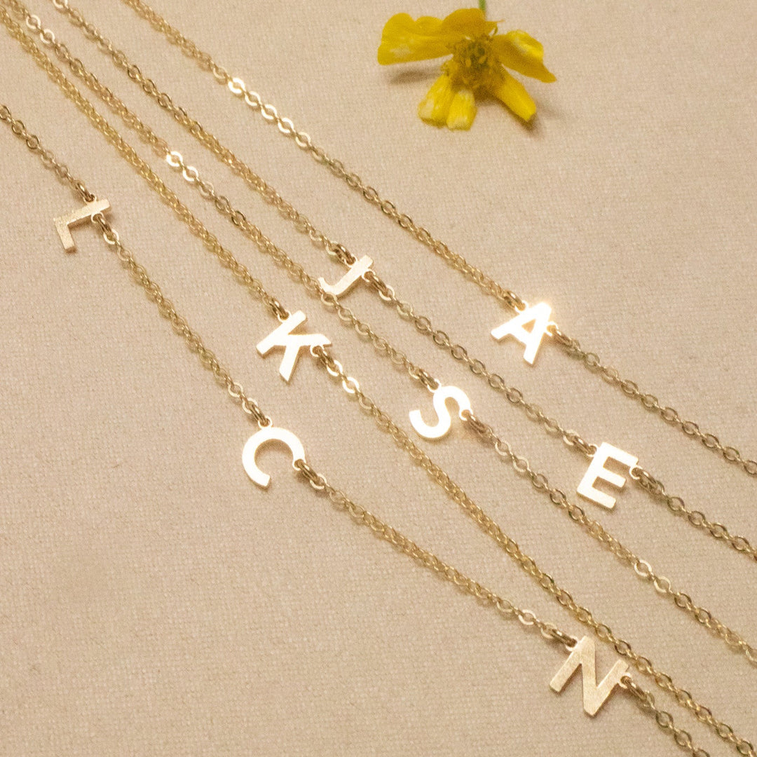 Gold necklaces with letter pendants on a beige background with yellow flowers.