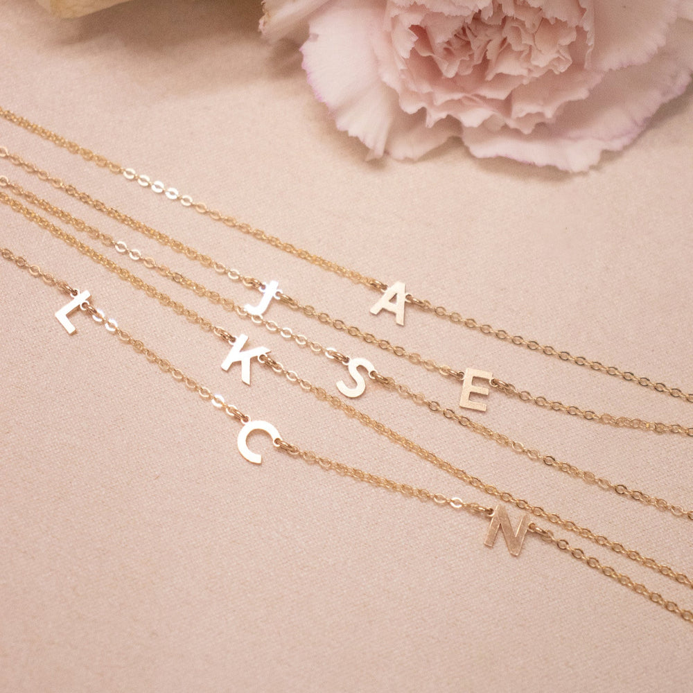 Gold necklaces with letter charms on a pink surface with flowers