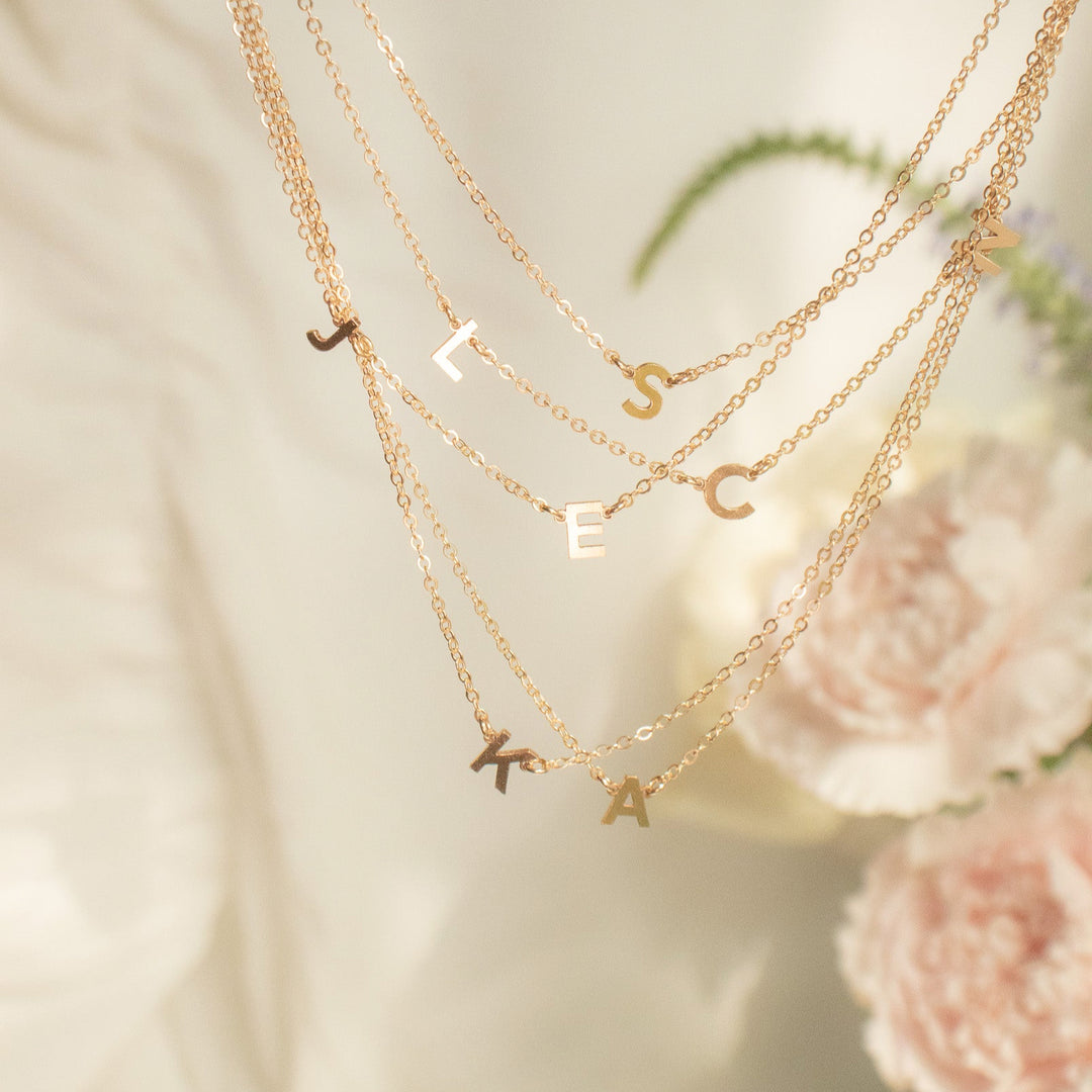 Three gold necklaces with various charms on a soft background with flowers.