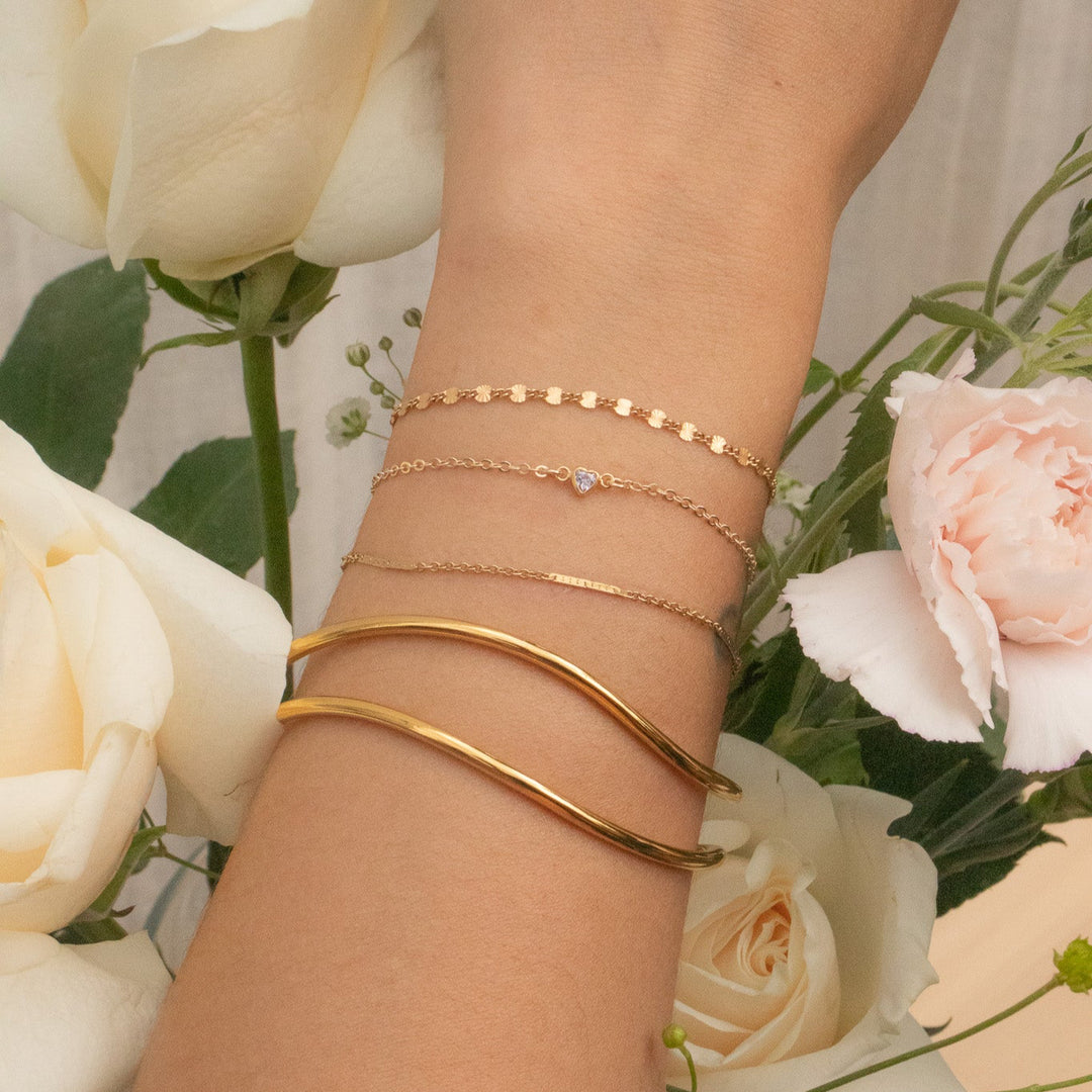 Gold bracelets on a wrist with flowers in the background