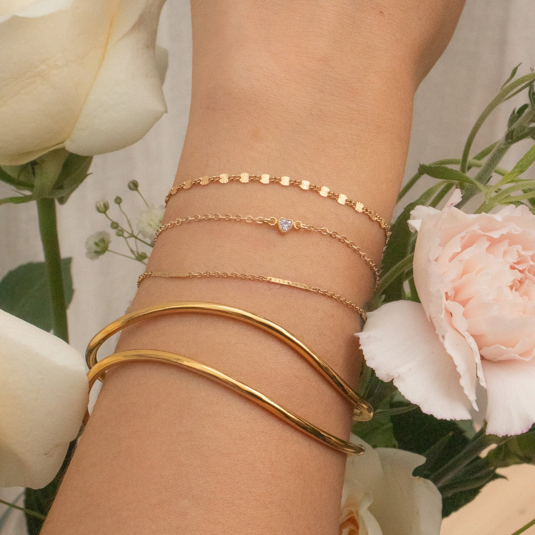 Gold bracelets on a wrist with flowers in the background