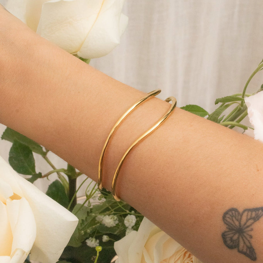 Gold bracelet on a wrist with white flowers in the background