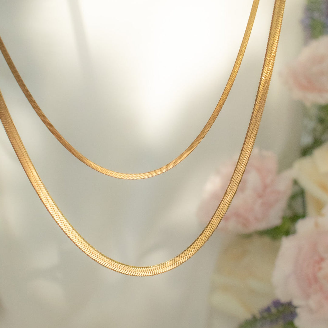 Gold necklace on a mannequin with a soft, blurred floral background