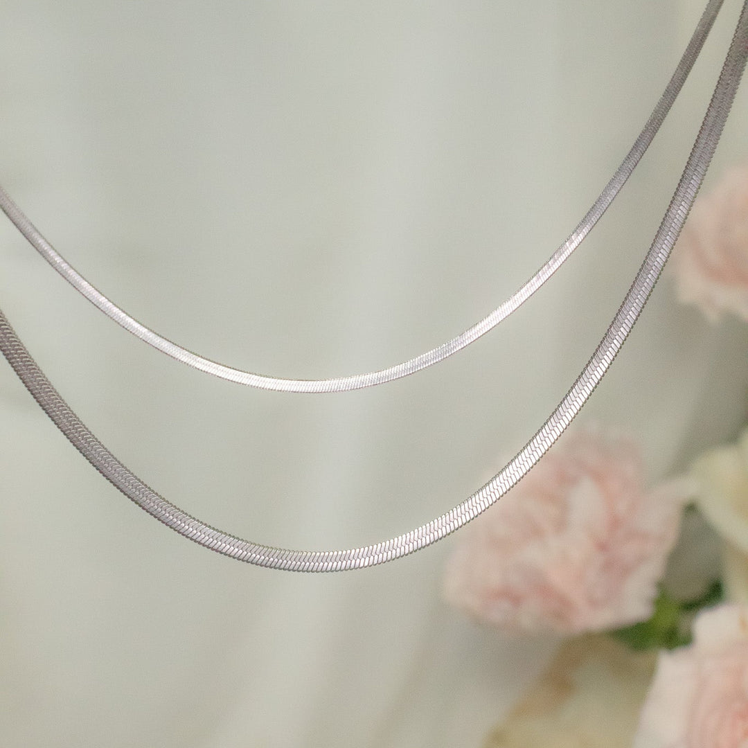Silver necklace on a light background with pink flowers