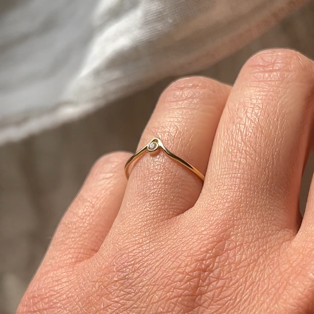 Close-up of a hand wearing a gold ring with a diamond on a neutral background
