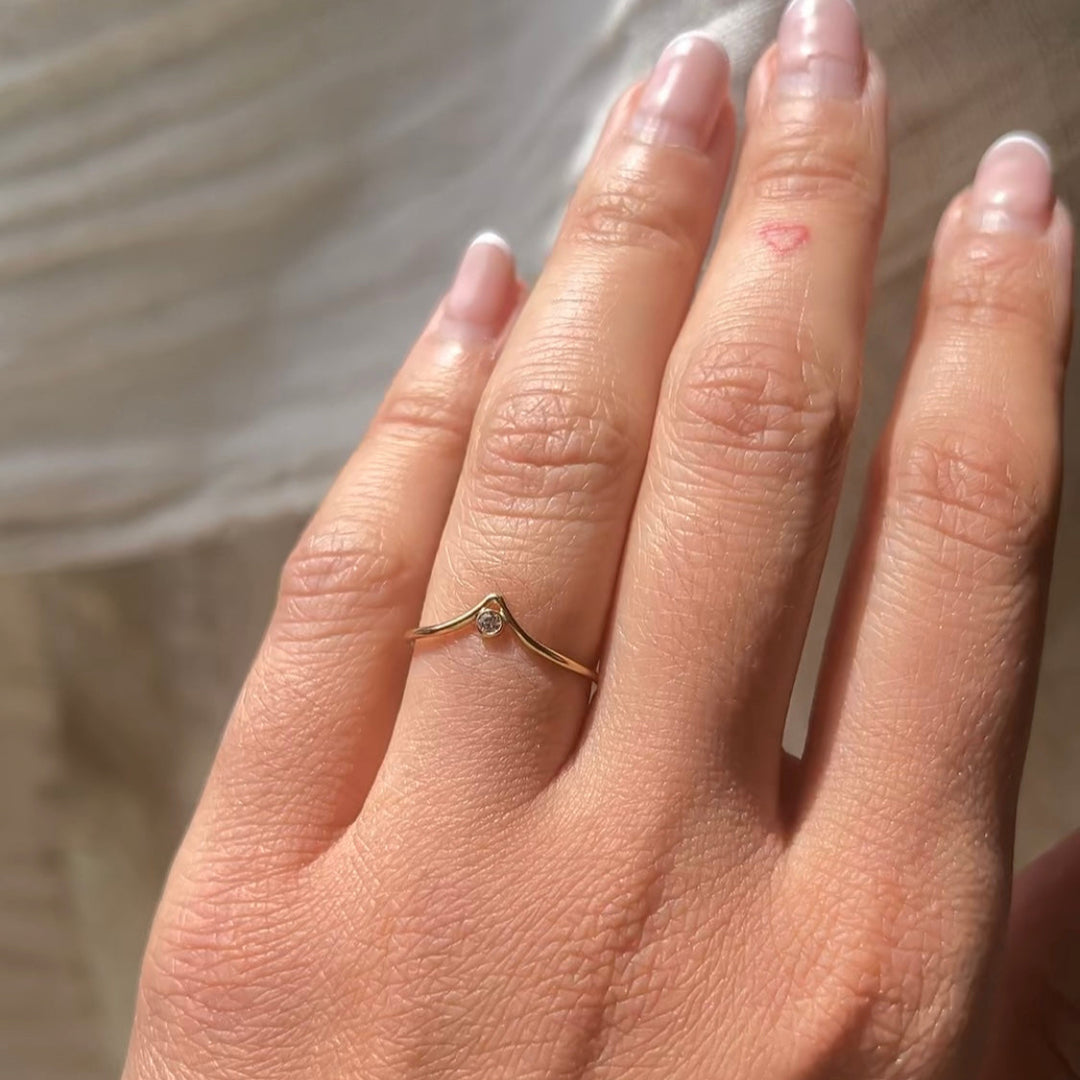Hand wearing a gold ring with a small diamond on a neutral background