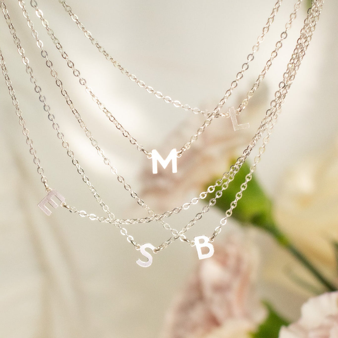Necklace with 'M S B' charms on a soft background with flowers