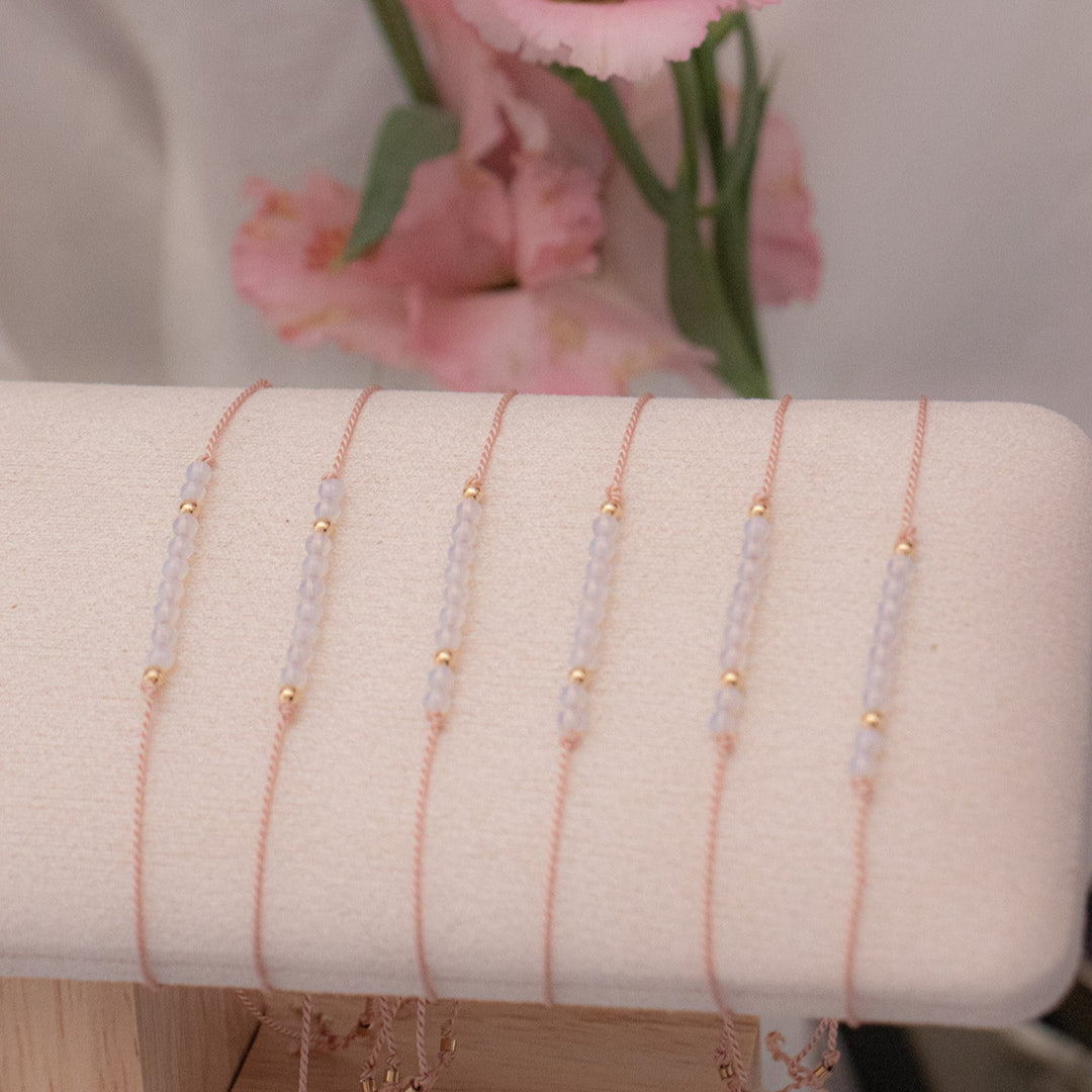 Beaded bracelets on a white cushion with pink flowers in the background