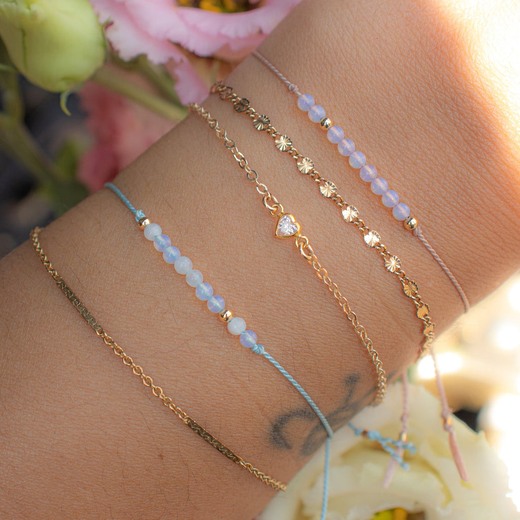 Close-up of a wrist with multiple gold and beaded bracelets against a floral background