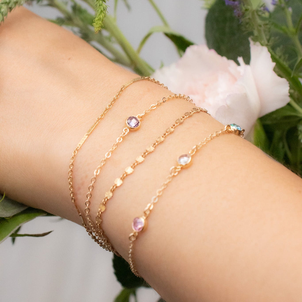 Close-up of a wrist wearing multiple gold bracelets with gemstones, against a natural background.