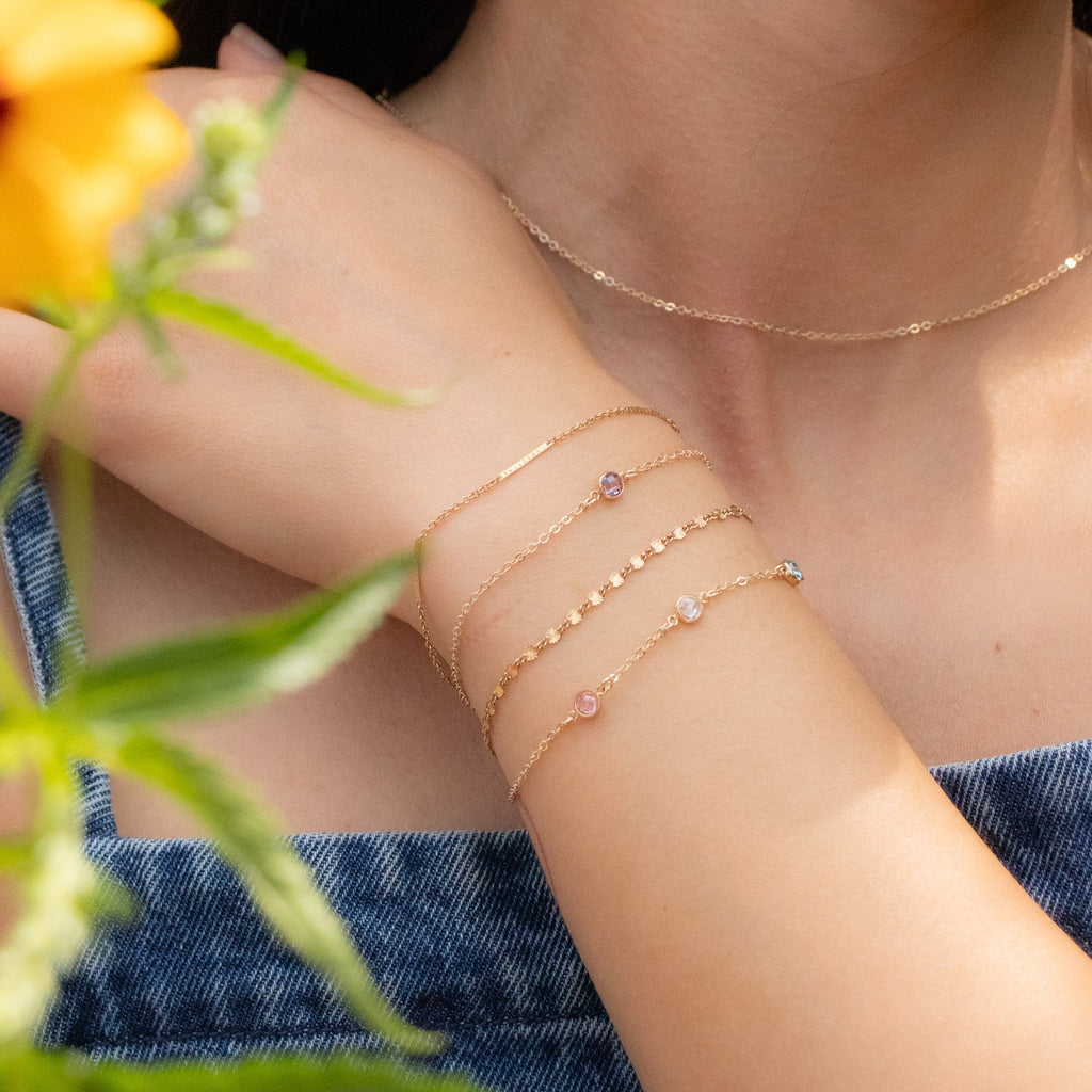 Close-up of a person's arm with gold bracelets and a necklace, holding a yellow flower.