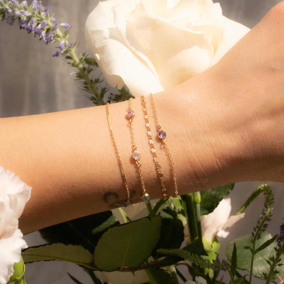 Hand wearing gold bracelets with a blurred background of flowers