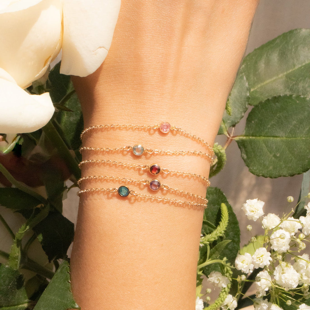 Close-up of a wrist wearing multiple gold bracelets with gemstones, surrounded by flowers.