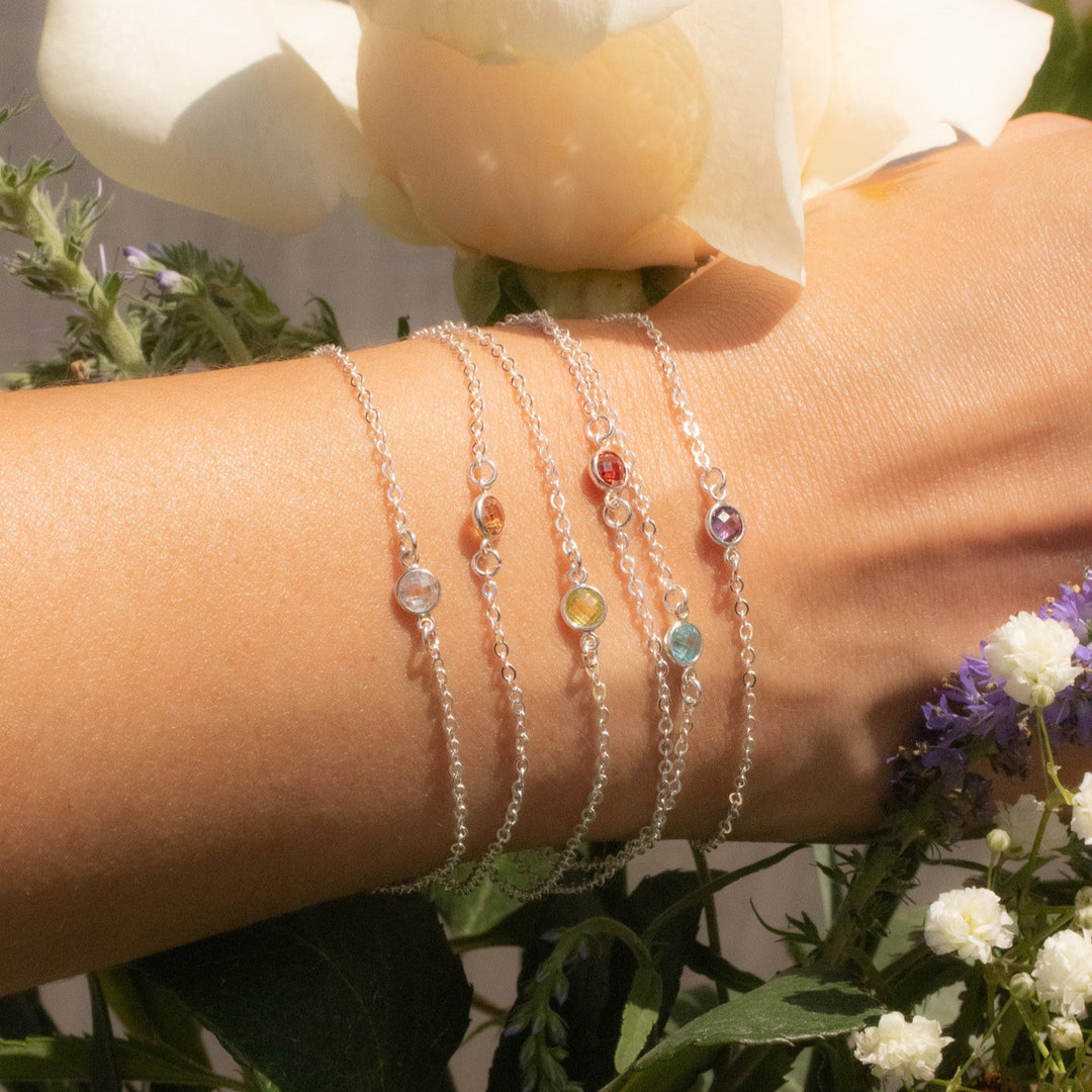 Hand wearing multiple silver bracelets with colorful beads against a floral background