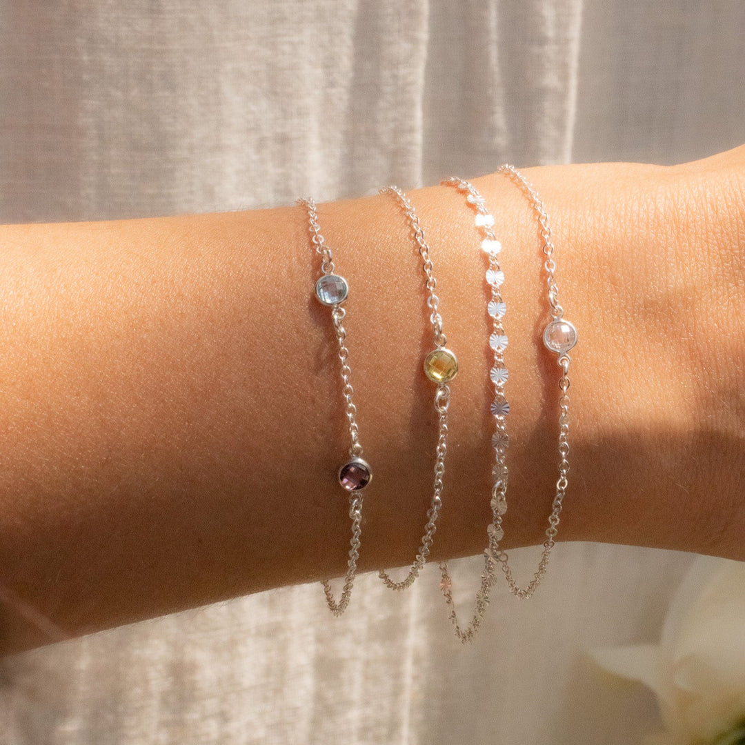 Close-up of a wrist wearing multiple delicate bracelets on a neutral background