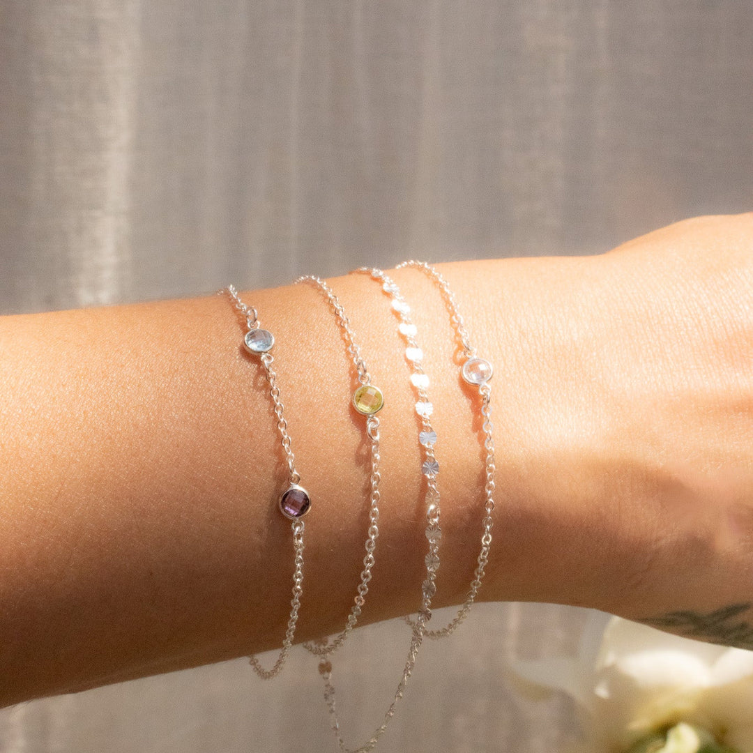 Close-up of a wrist wearing multiple silver bracelets with small beads against a neutral background