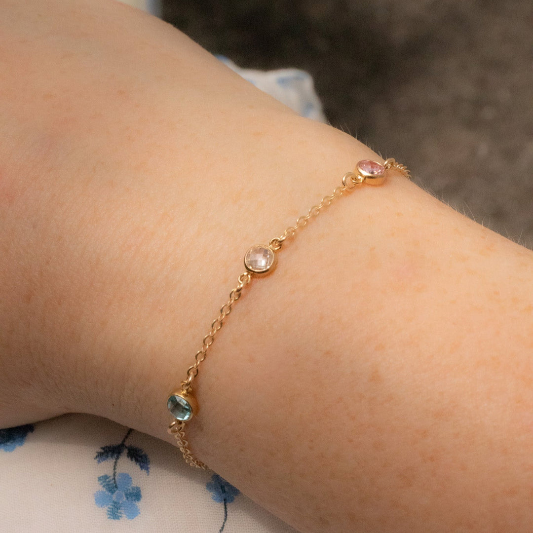 Gold bracelet with small gemstones on a wrist against a floral-patterned fabric background
