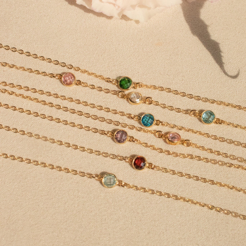 Gold bracelets with colorful gemstones on a beige surface with a pink flower.