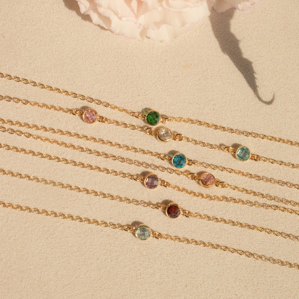 Gold bracelets with gemstones on a beige surface with pink flowers in the background