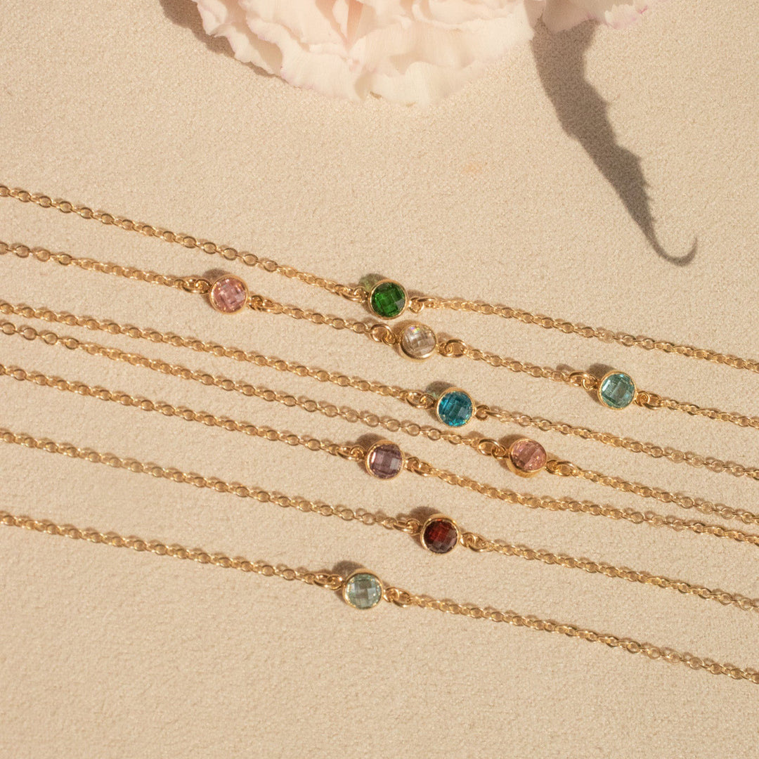 Gold bracelets with gemstones on a beige surface with pink flowers in the background