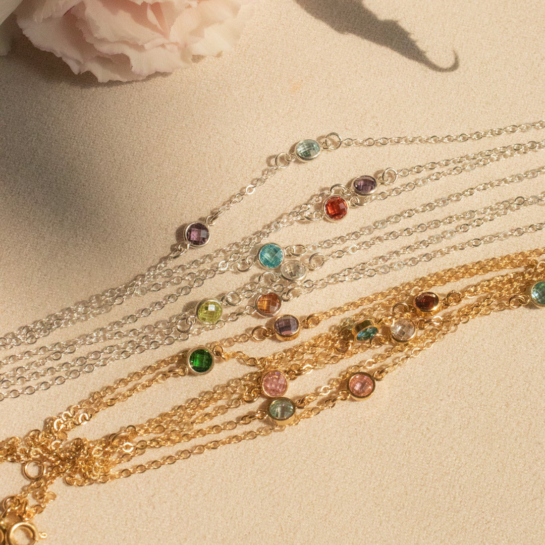 Gold bracelets with colorful gemstones on a light surface with a pink flower and green leaves.