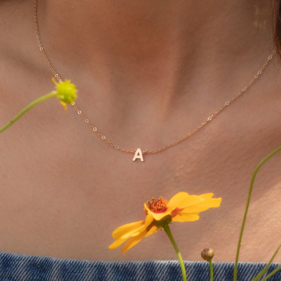 Necklace with a letter 'A' pendant worn by a person with yellow flowers in the foreground.