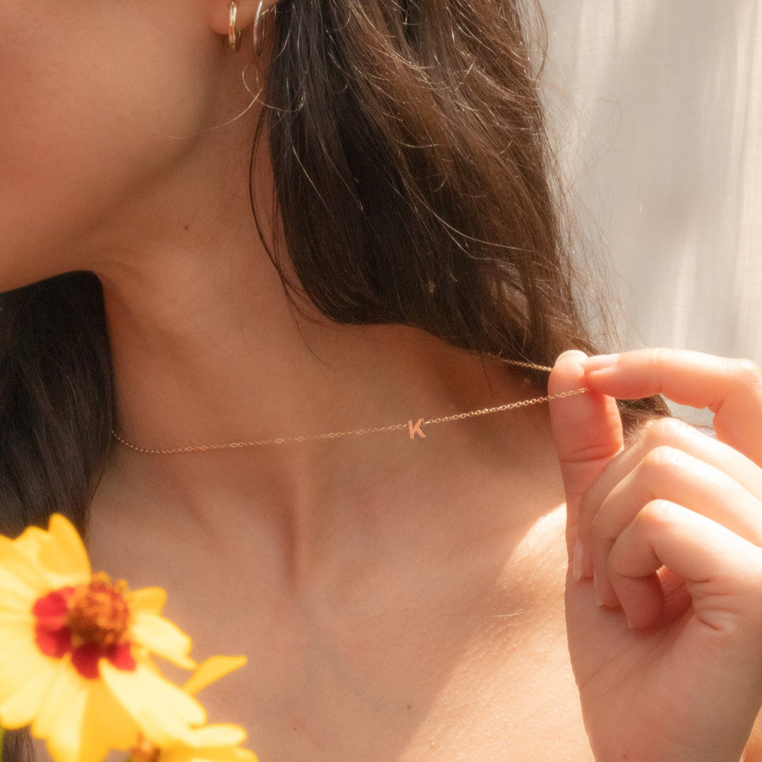 Person wearing a delicate gold necklace with a small pendant, holding a yellow flower.