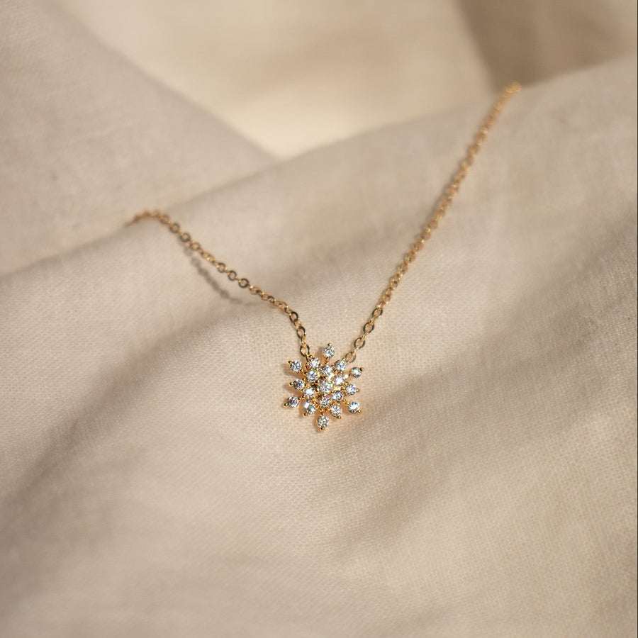 Gold necklace with a snowflake pendant on a neutral background