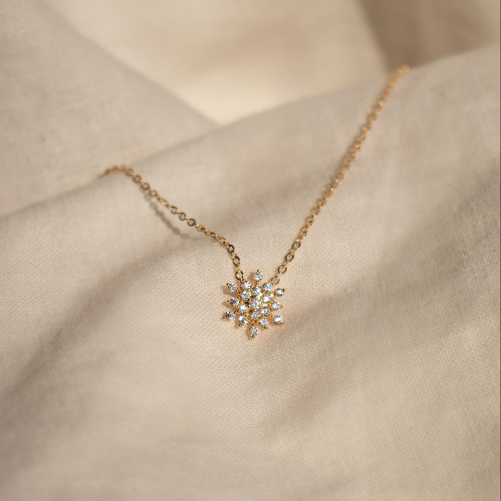 Gold necklace with a snowflake pendant on a neutral background