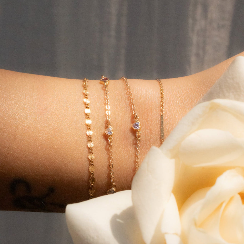 Gold bracelets on a wrist with a white rose in the foreground
