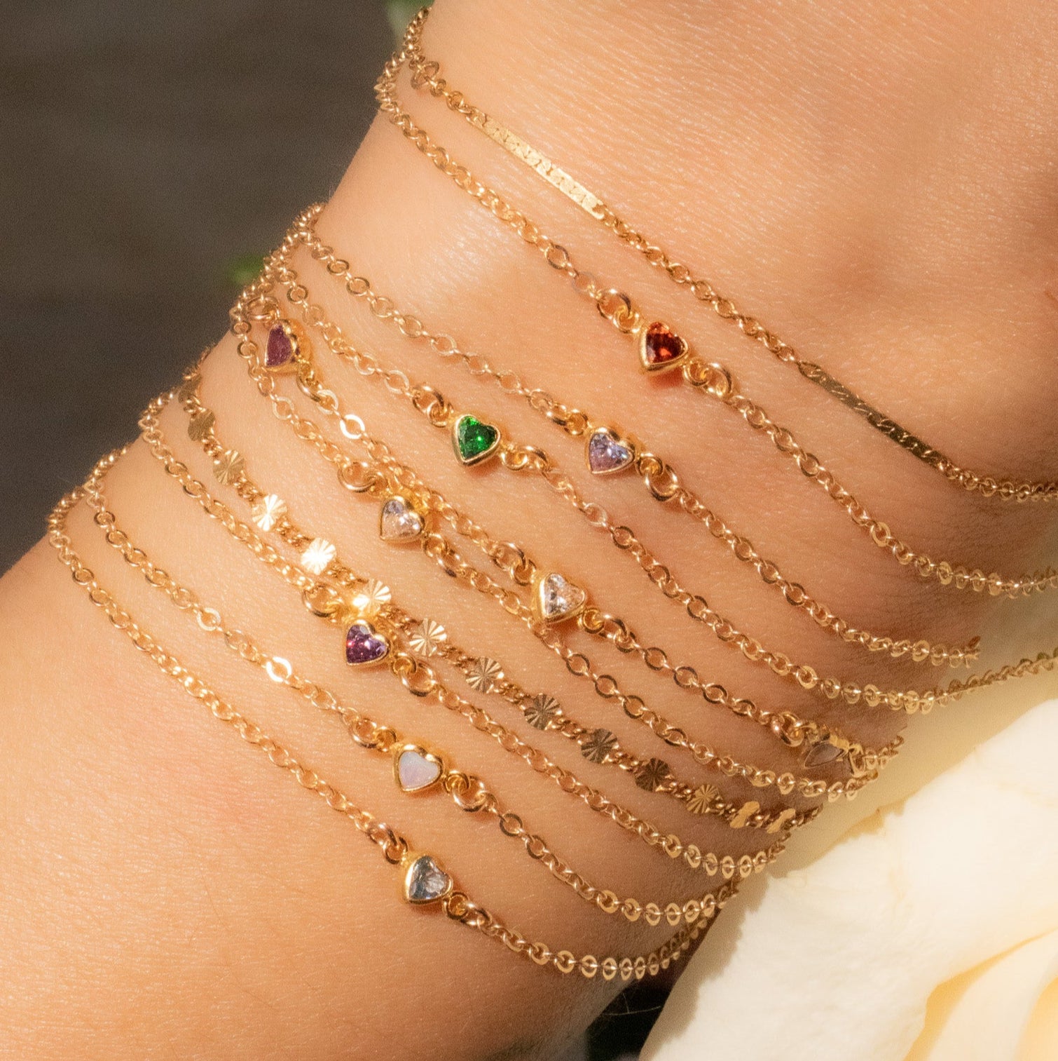 Multiple gold bracelets with heart-shaped charms on a wrist, with a blurred background.