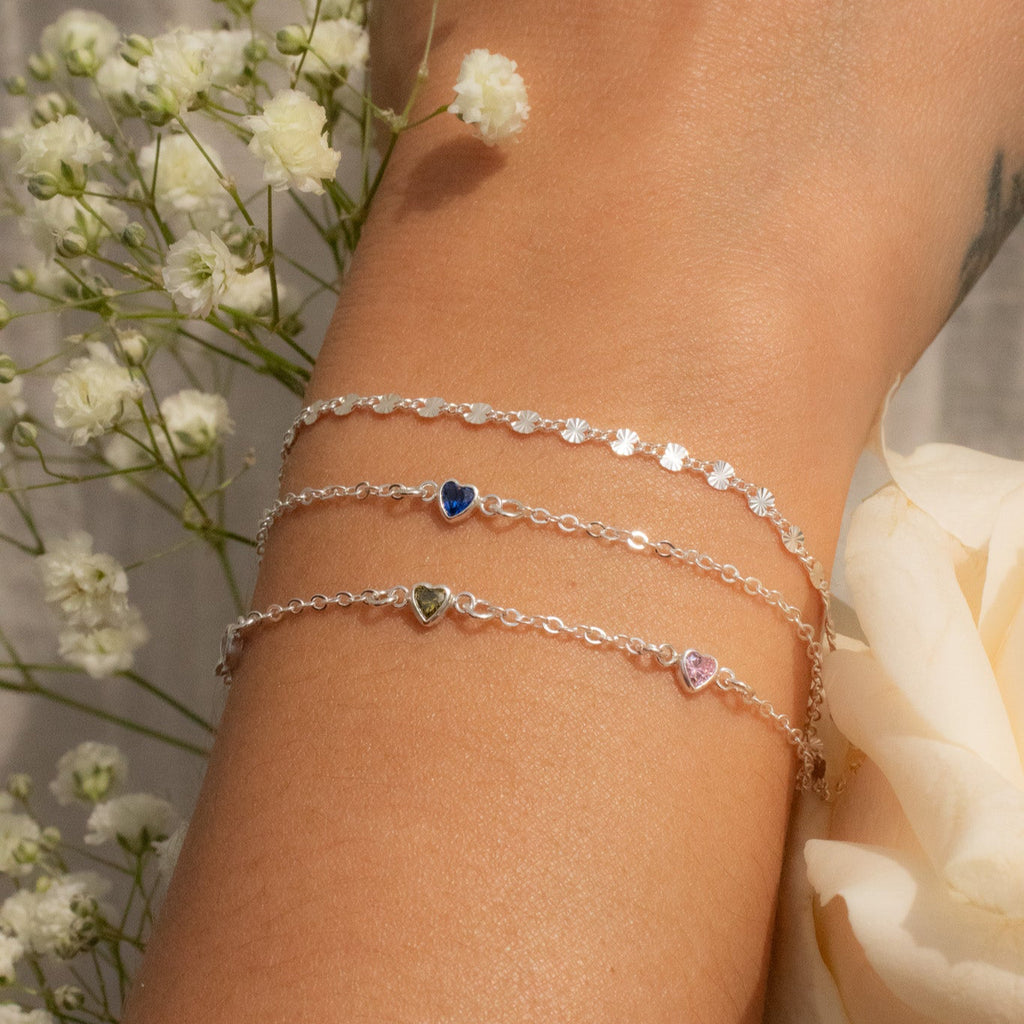 Close-up of a wrist wearing multiple bracelets with flowers in the background