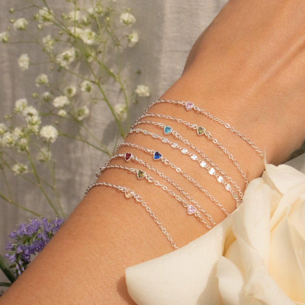 Close-up of a wrist wearing multiple silver bracelets with flowers in the background