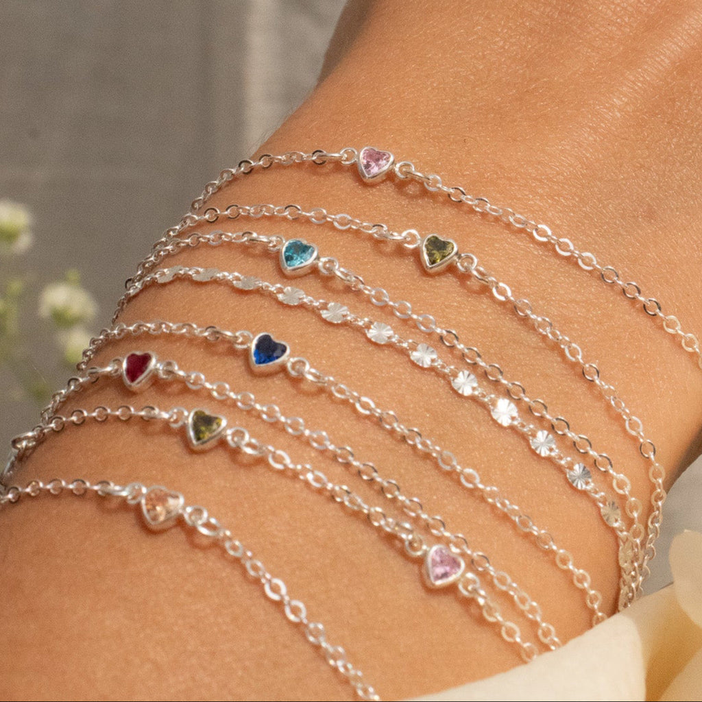 Multiple bracelets with heart-shaped charms on a wrist, with a blurred background