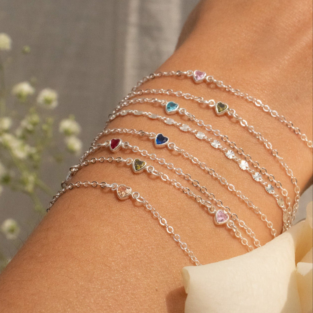 Close-up of a person's arm wearing multiple silver bracelets with heart charms against a blurred natural background.