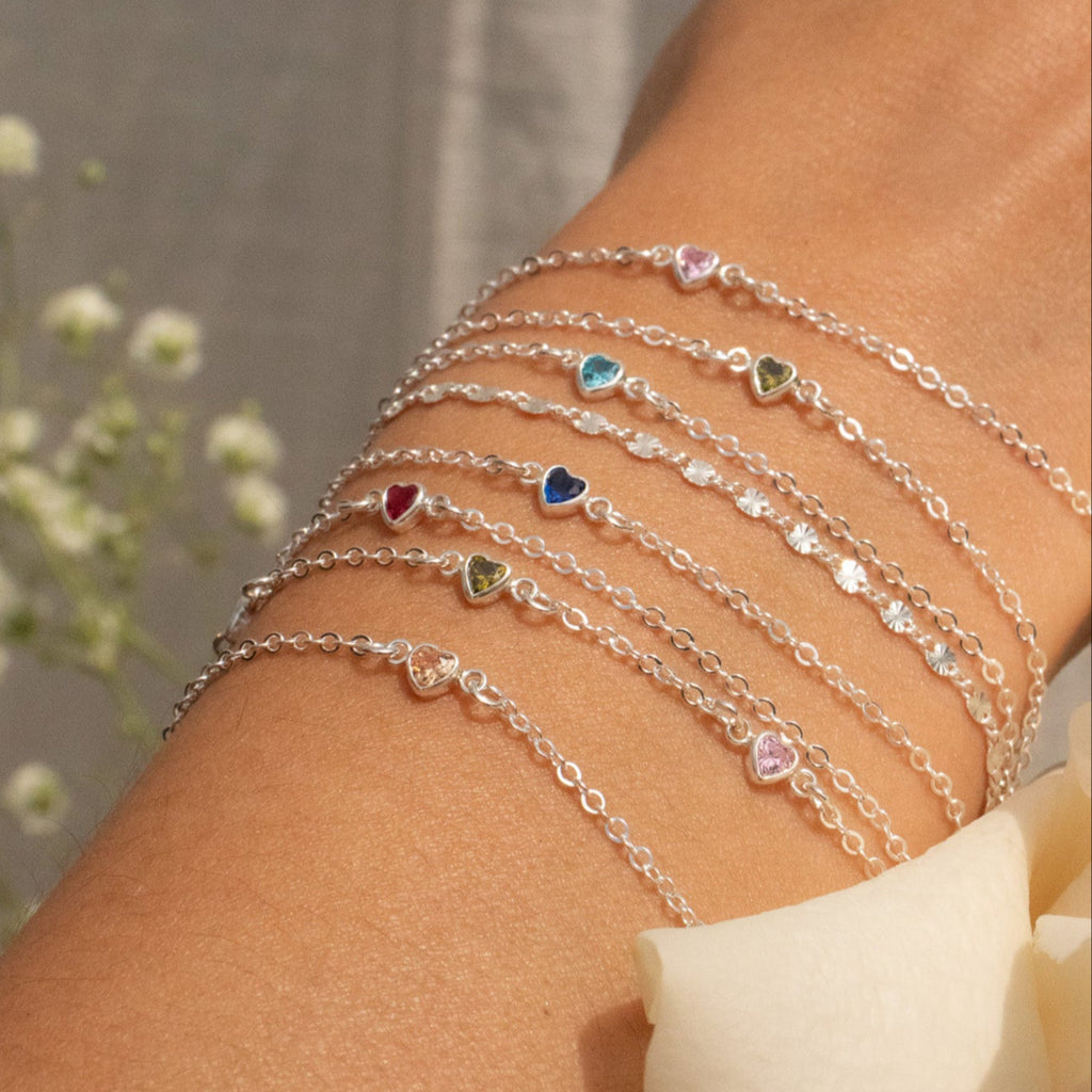 Close-up of a person's arm wearing multiple silver bracelets with heart charms against a blurred natural background.