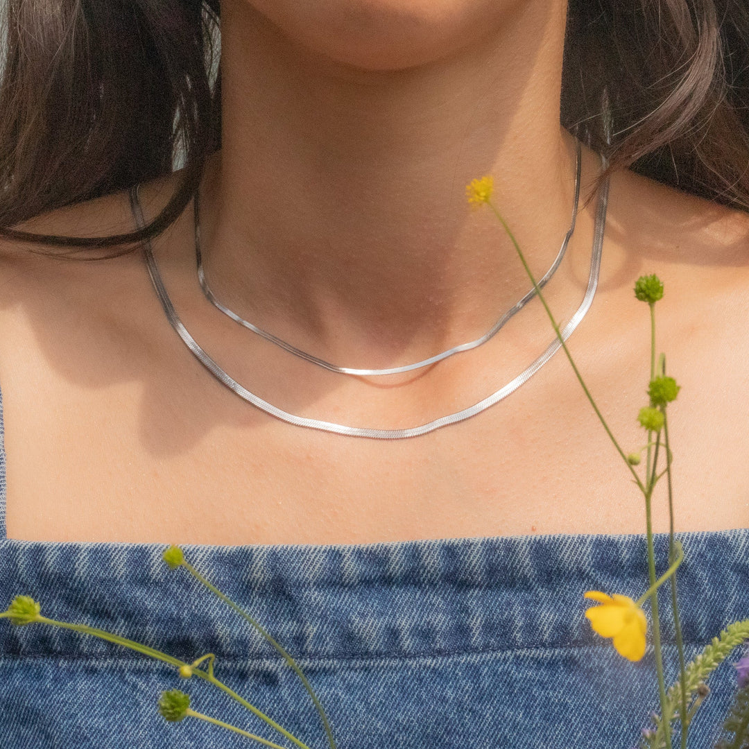 Silver necklace worn by a person with a denim top and flowers in the background
