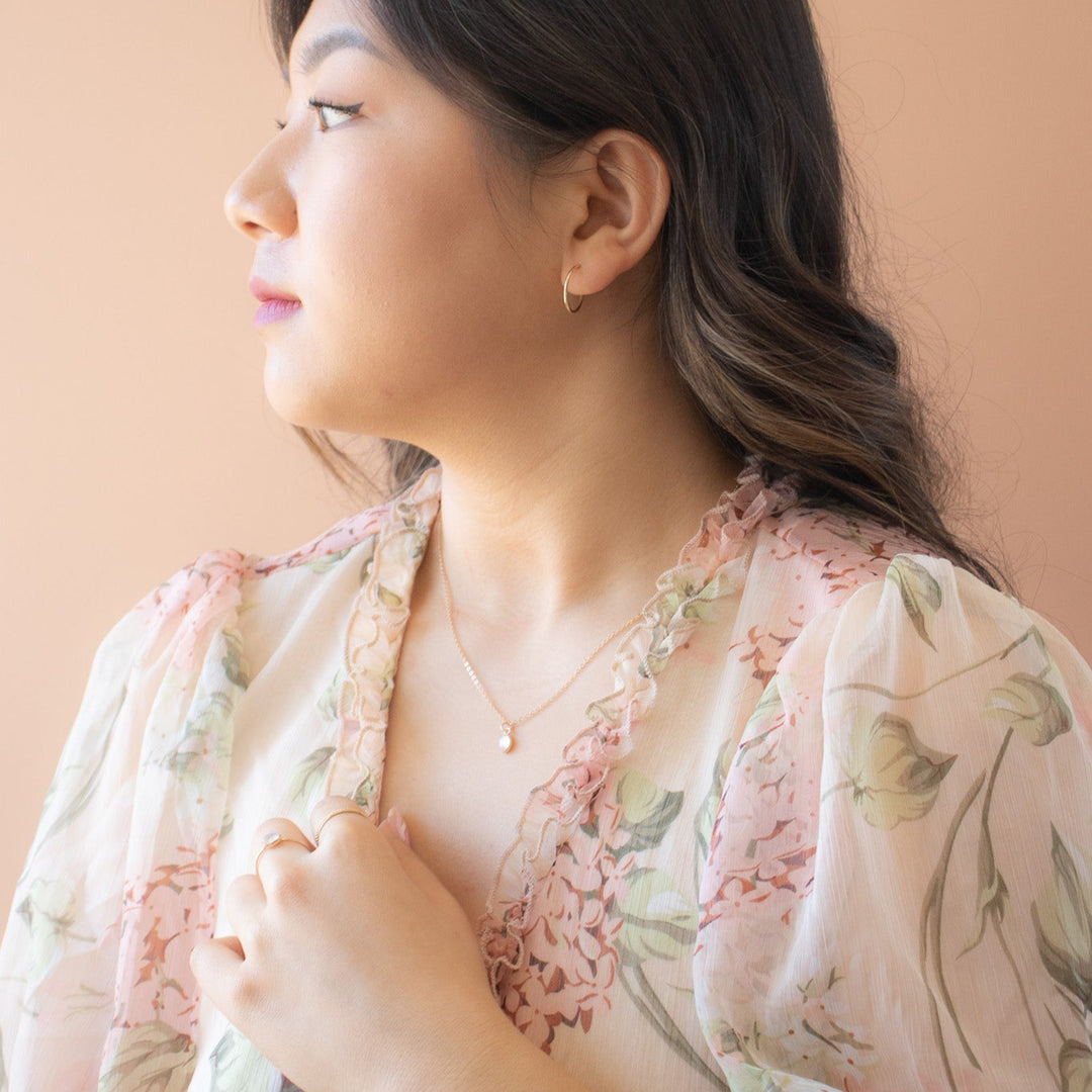 Woman wearing a floral dress against a beige background with a delicate oval moonstone necklace