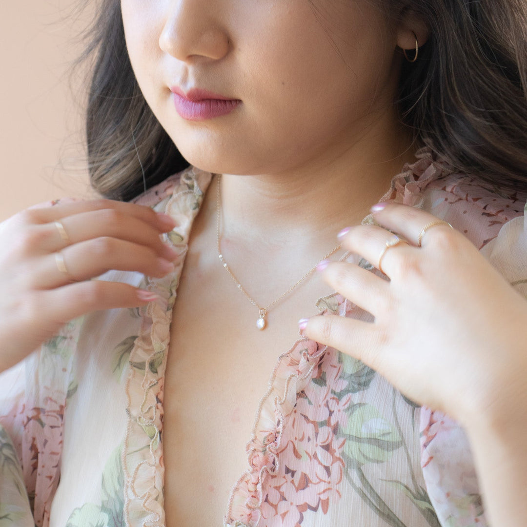 Woman wearing a floral outfit and necklace, adjusting her clothing.