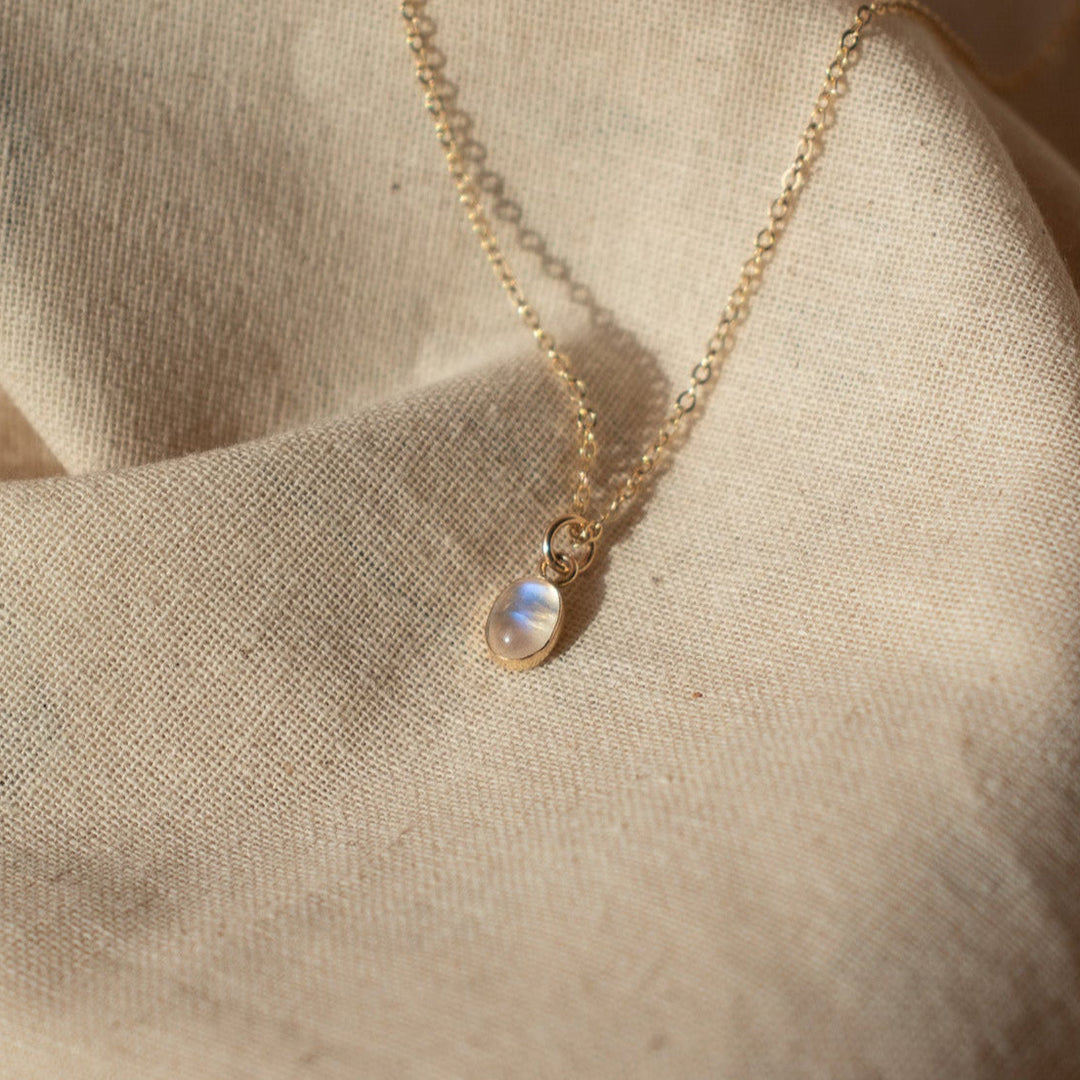 Gold necklace with a small pendant on a beige fabric background