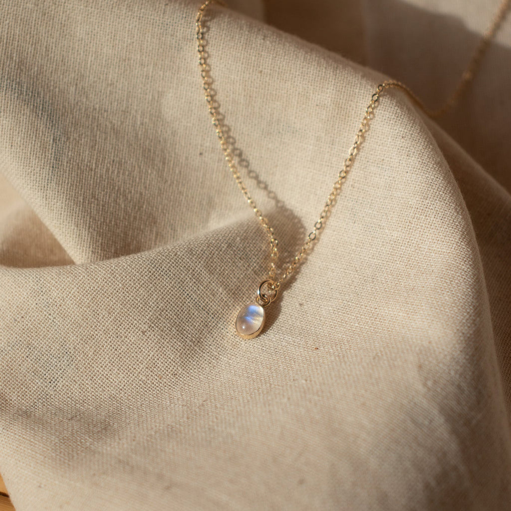Gold necklace with a small pendant on a beige fabric background