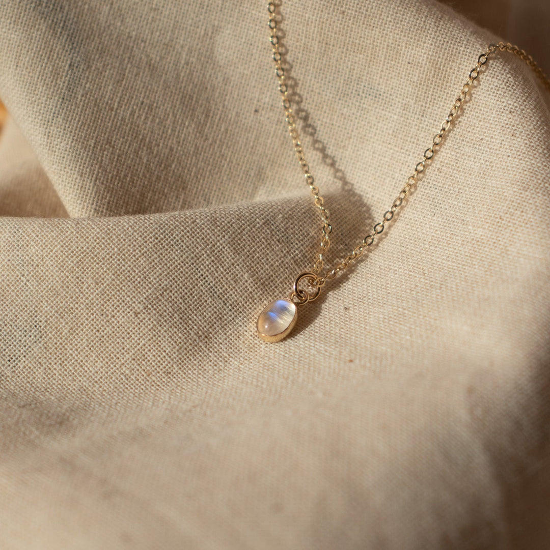 Delicate gold moonstone necklace with a small pendant on a textured beige fabric background