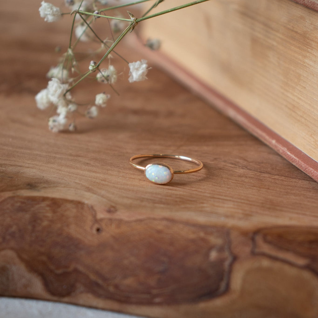 Gold ring with a white stone on a wooden surface with small white flowers.