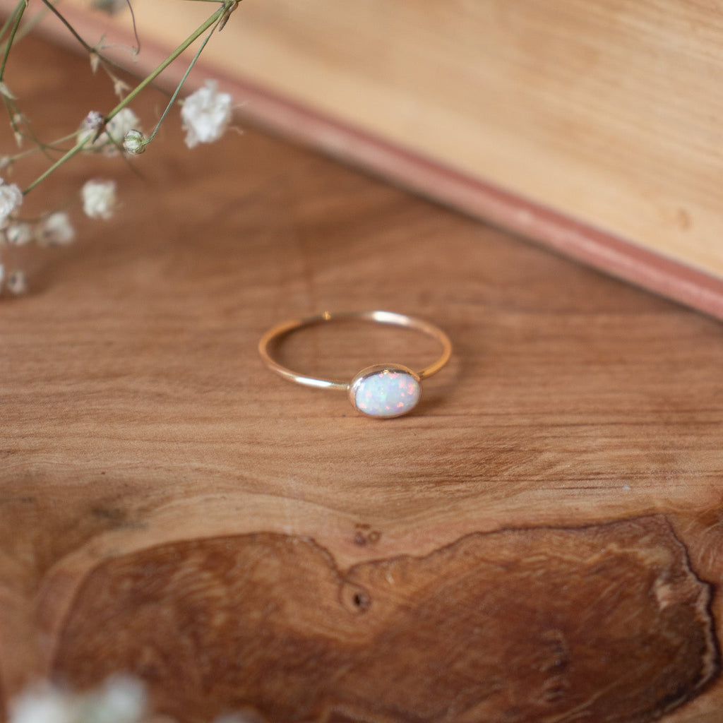 Gold ring with a white stone on a wooden surface with dried flowers.