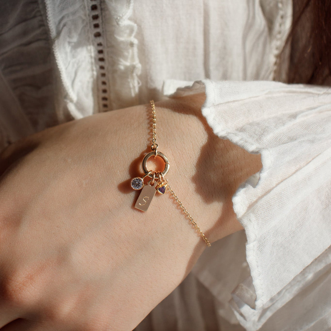 Close-up of a hand wearing a gold bracelet with charms against a white lace garment.