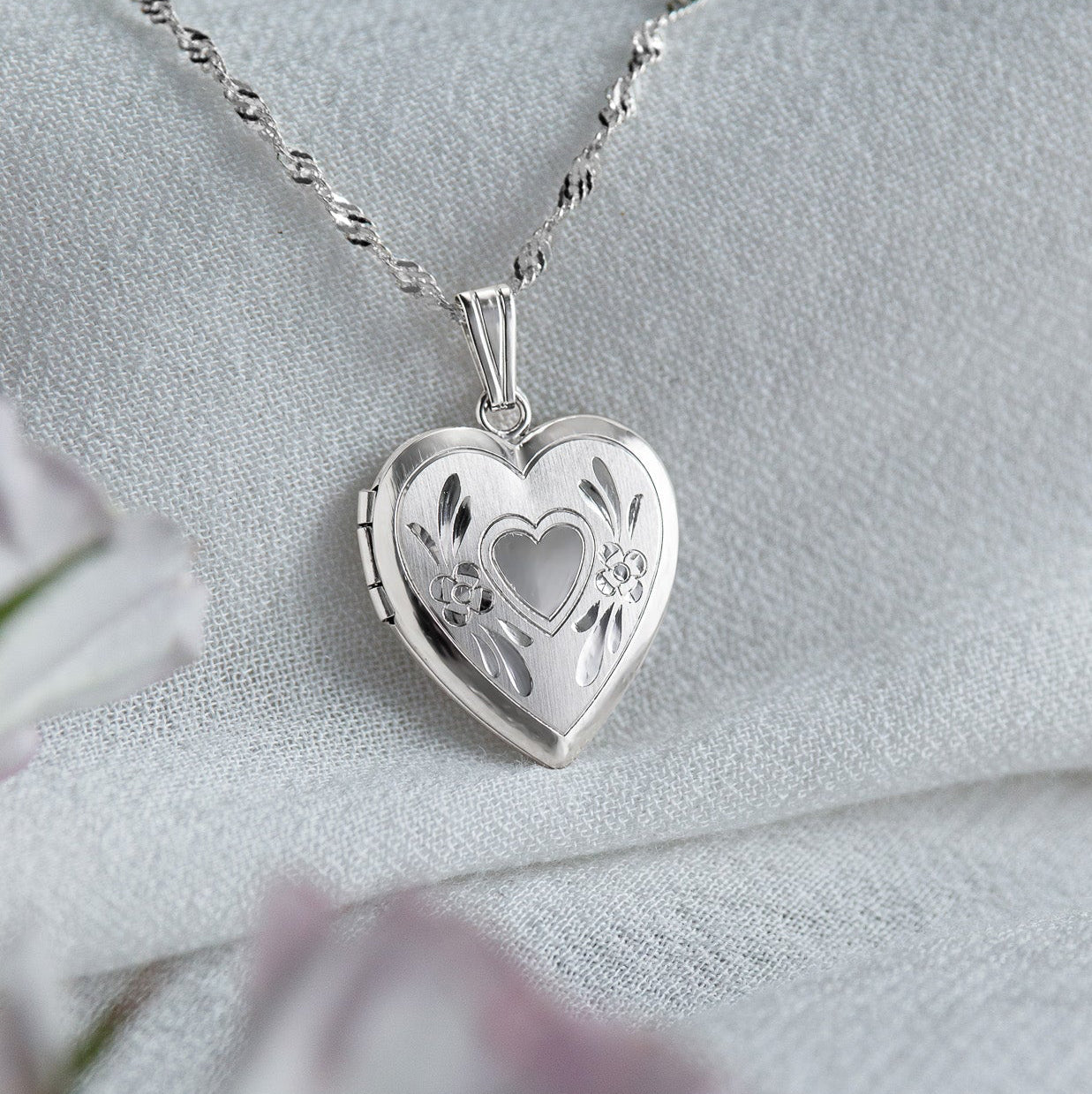 Silver heart-shaped locket on a chain with a soft white background